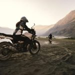 Motociclista y pasajero con casco certificado y equipo de protección rodando en carretera